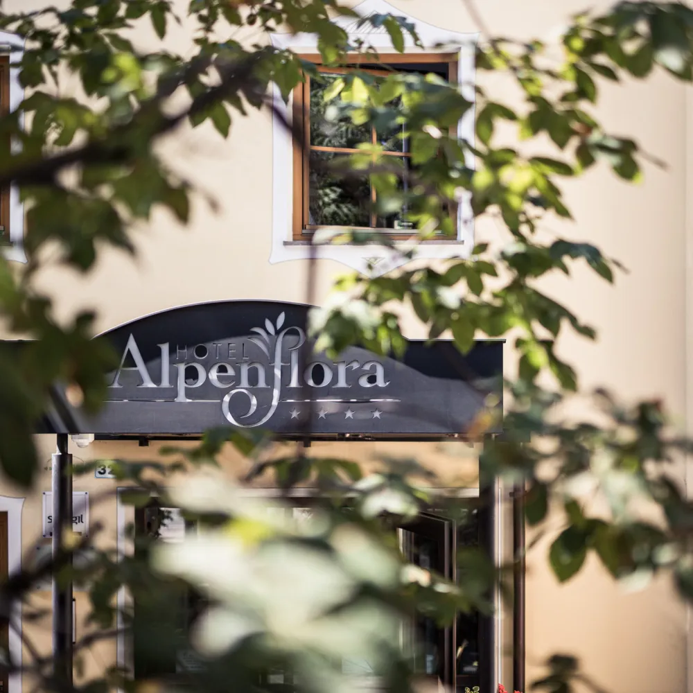 Fassade des Hotels Alpenflora mit Schriftzug, von grünen Blättern gerahmt