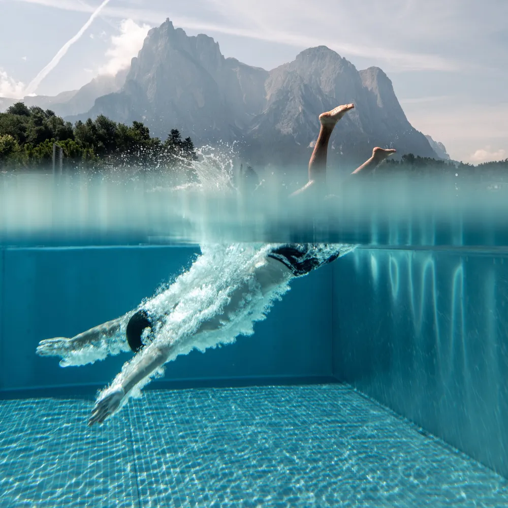 Schwimmer im Infinity-Pool des Alpenflora mit Unterwasserblick und Schlern im Hintergrund