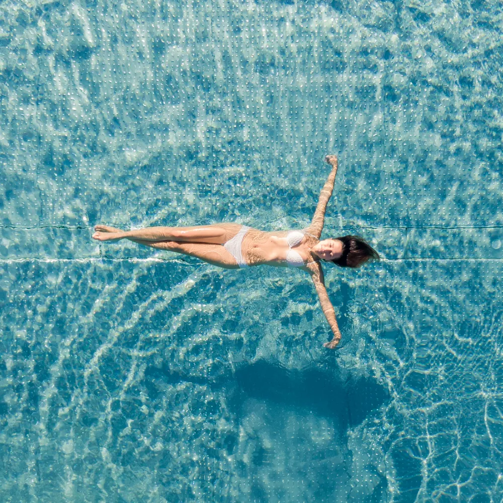 Frau schwebt entspannt rücklings im türkisfarbenen Pool des Wellnesshotels Alpenflora