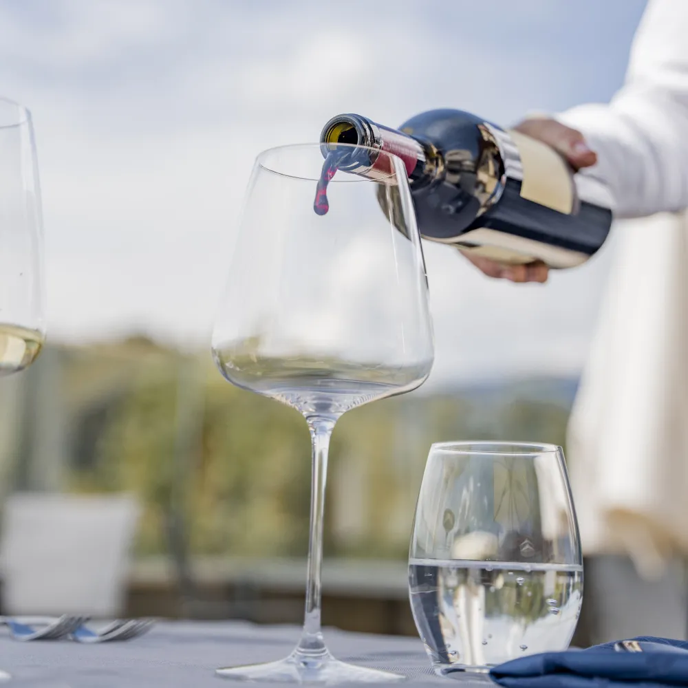 Rotwein wird ins Glas eingeschenkt, dazu ein Wasserglas auf der Terrasse des Alpenflora