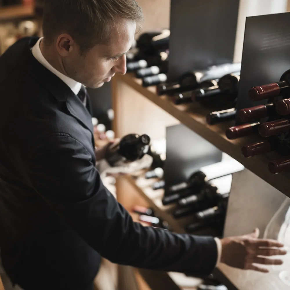 Sommelier des Alpenflora greift eine Flasche aus dem dunklen Weinregal