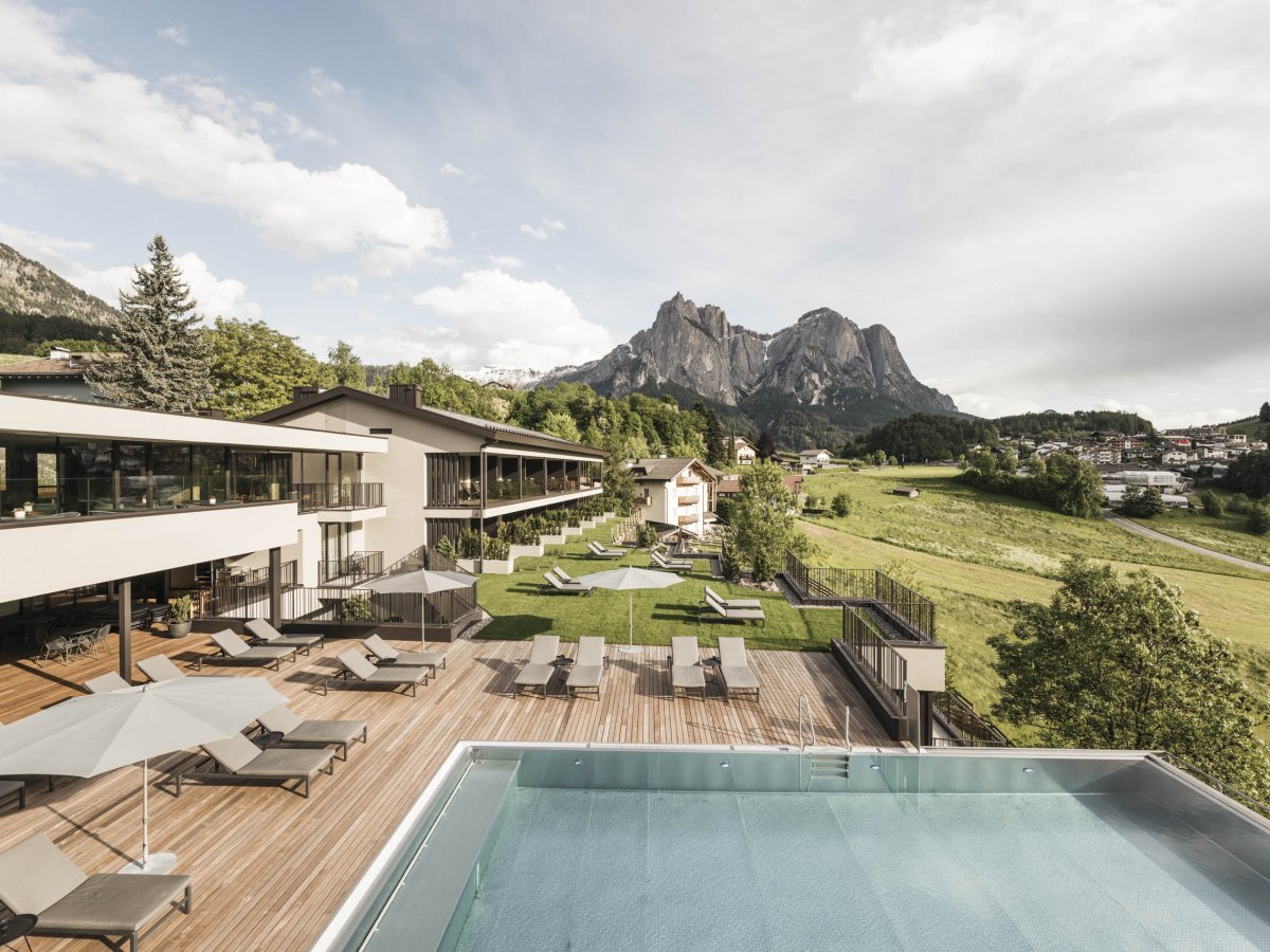 Sommeransicht des Wellnesshotels Alpenflora mit Sonnenterrasse, Pool und Blick auf die Berge