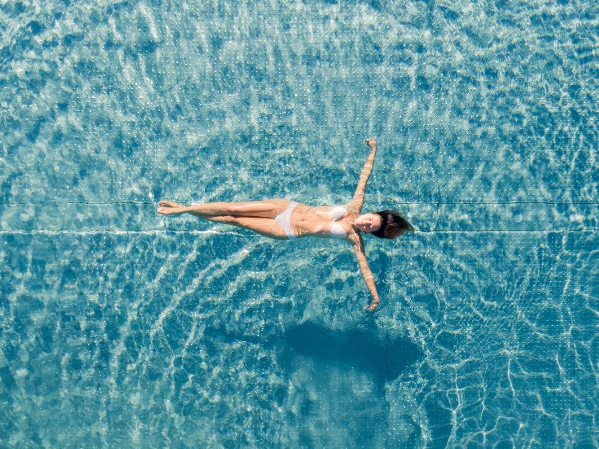 Frau schwebt entspannt rücklings im türkisfarbenen Pool des Wellnesshotels Alpenflora