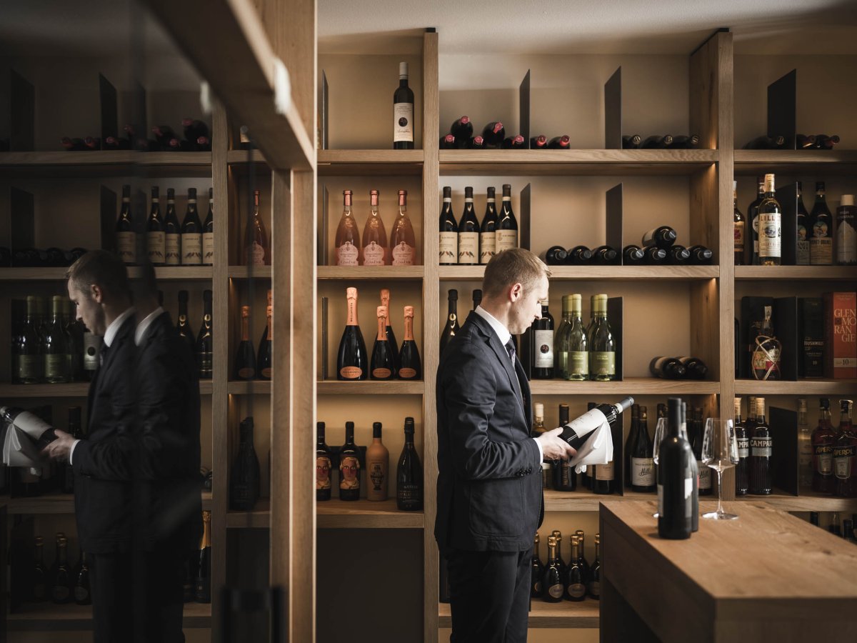 Sommelier wählt im Weinkeller eine Flasche aus den gut gefüllten Holzregalen aus
