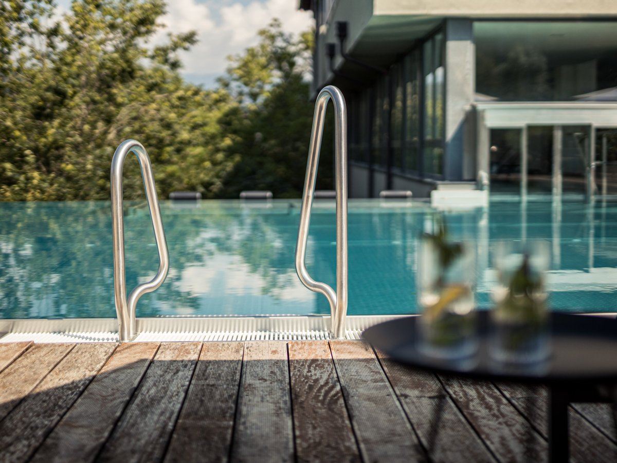 Edelstahl-Einstieg in den Außenpool mit Holzdeck und Getränken im Wellnesshotel Alpenflora