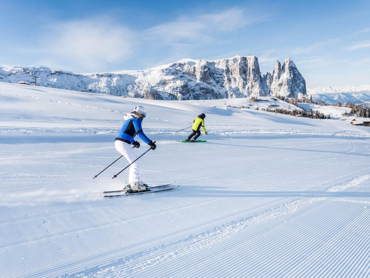 Zwei Skifahrer auf frisch präparierter Piste vor dem Bergpanorama der Dolomiten bei Kastelruth.