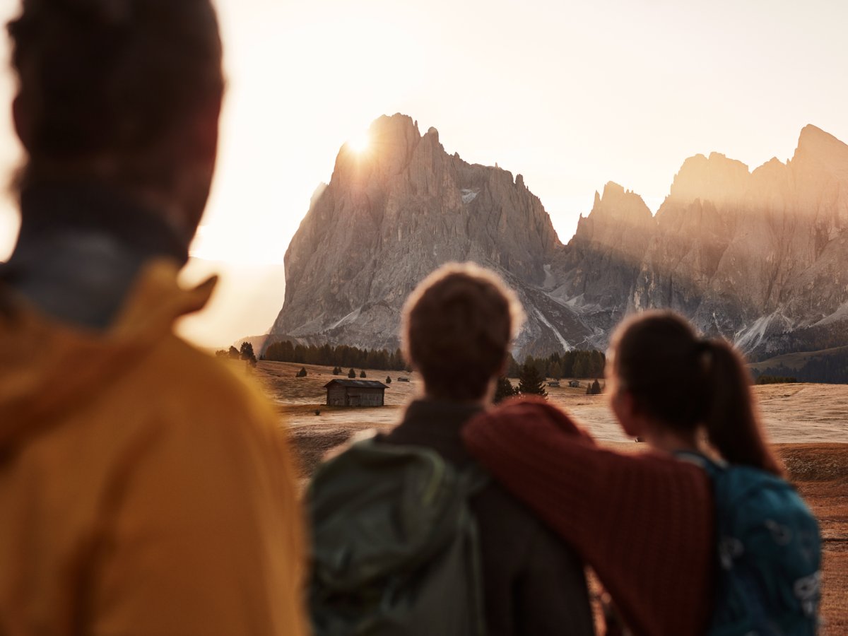 Wanderer blicken auf der Seiser Alm im Herbst zum Sonnenaufgang über den Dolomitengipfeln.