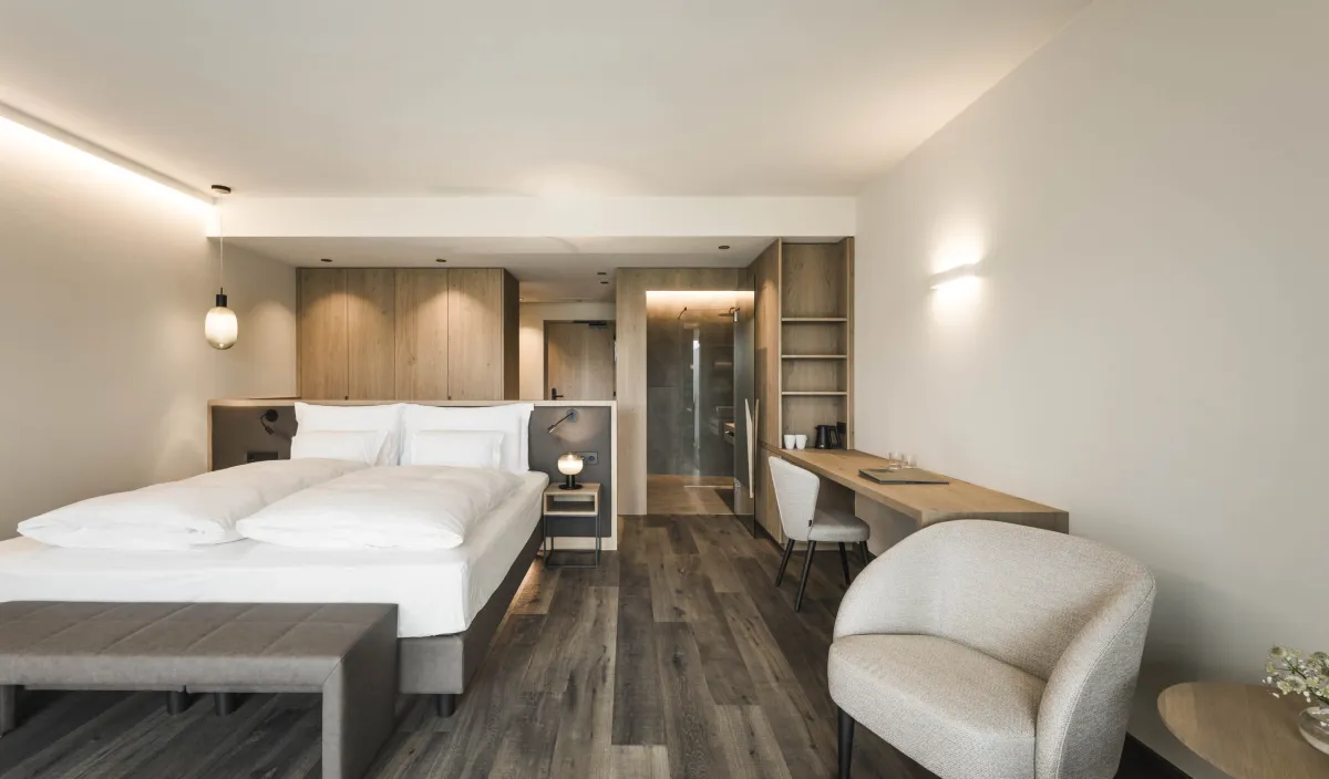 Doppelzimmer Garden View im Wellnesshotel Alpenflora mit Doppelbett, Schreibtisch, Sessel und einsehbarer Dusche.