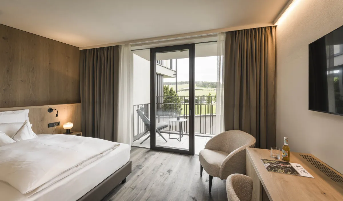 Einzelzimmer Garden Single Stay im Wellnesshotel Alpenflora mit Bett, Sessel, Schreibtisch und Balkon mit Blick ins Grüne.