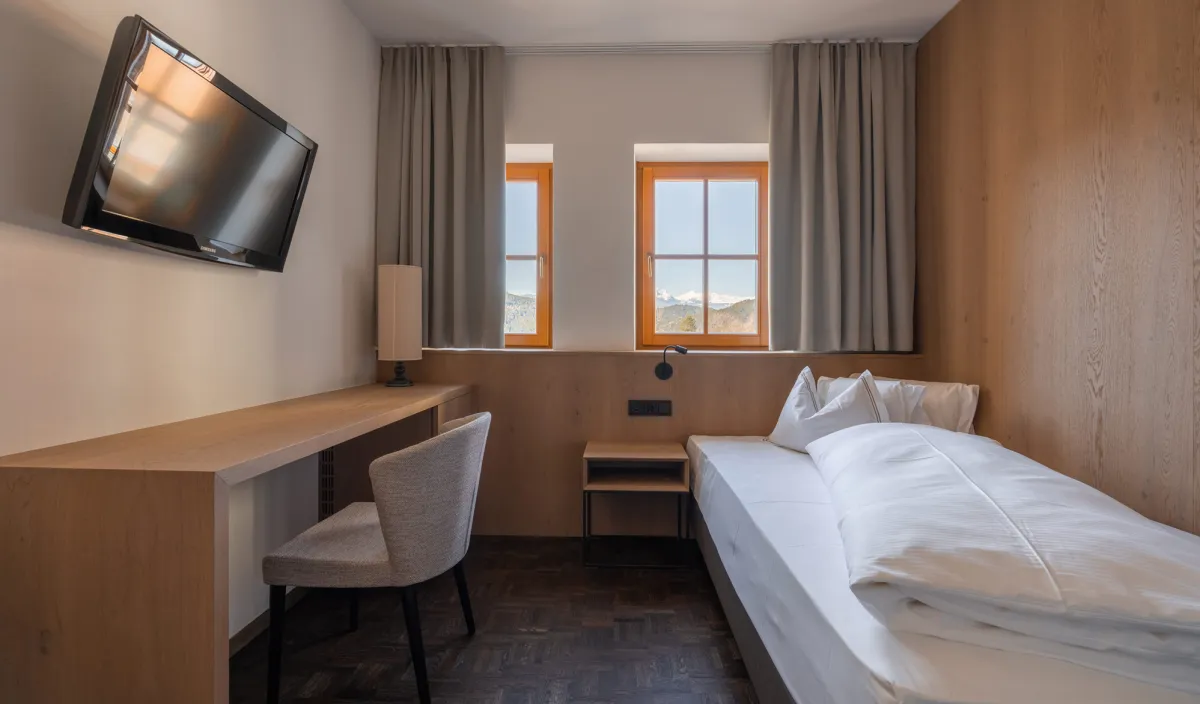 Einzelzimmer Single Stay im Wellnesshotel Alpenflora mit Bett, Schreibtisch, Fernseher und Fenstern mit Bergblick.