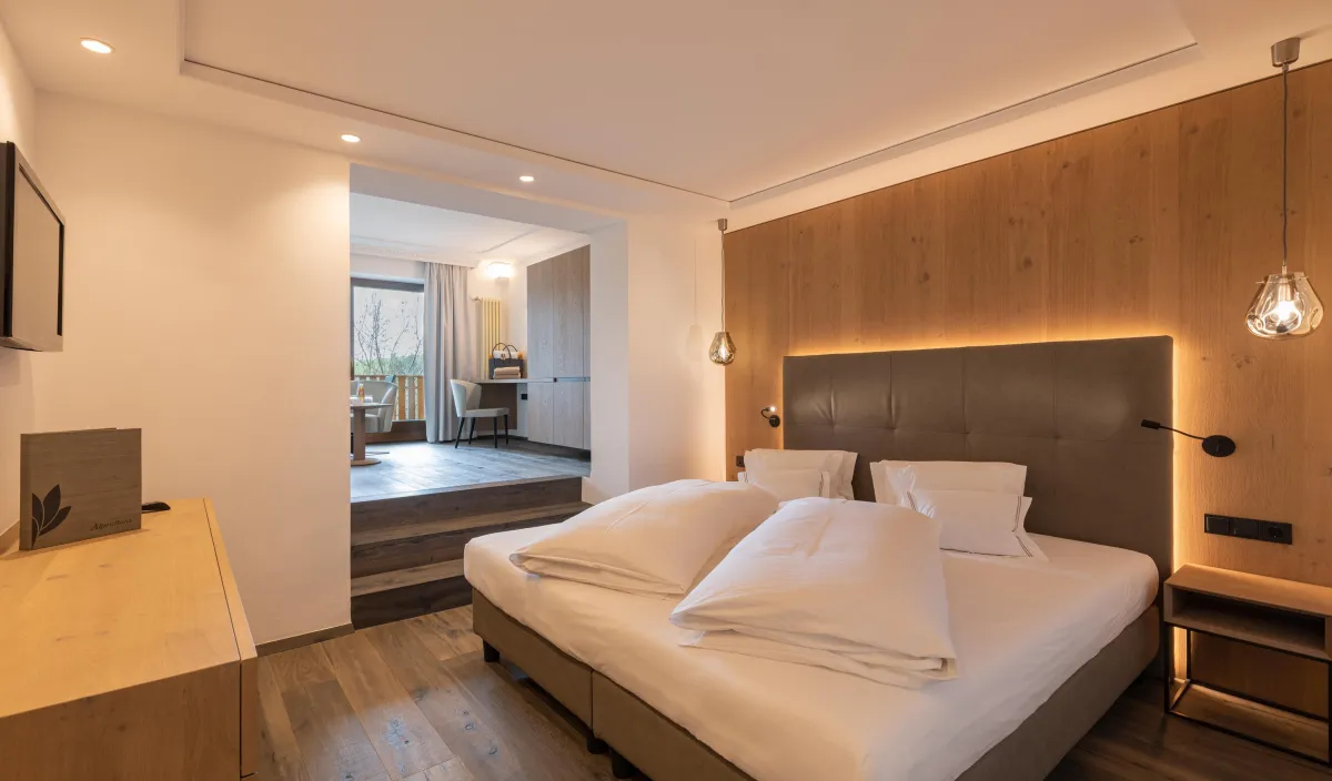 Schlafbereich der Sun Suite im Wellnesshotel Alpenflora mit Doppelbett, Holzwandverkleidung und Durchgang zum Wohnraum.