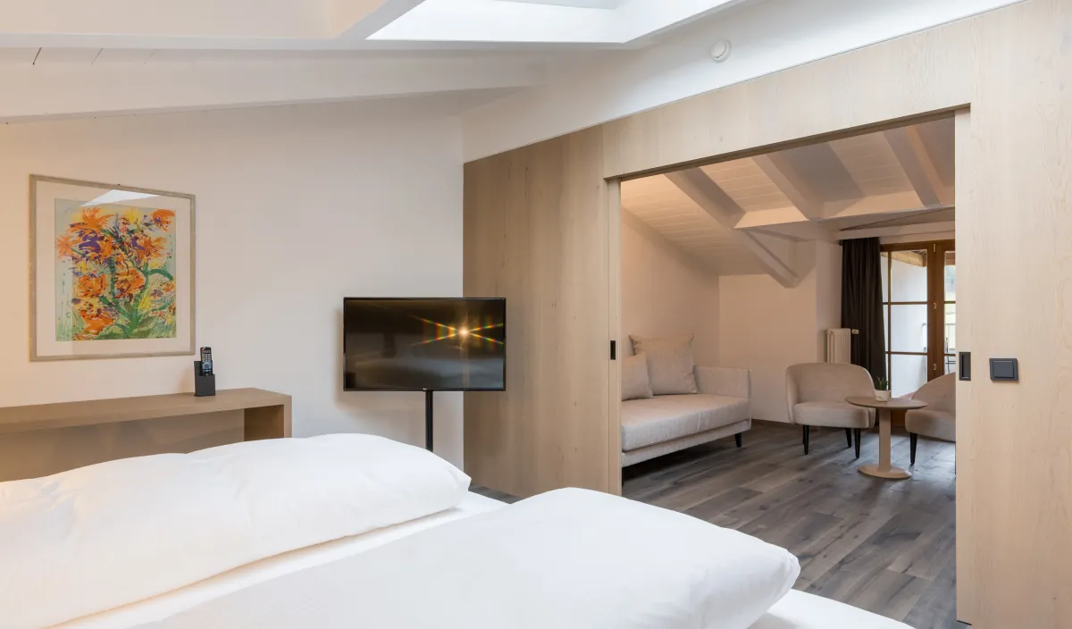 Blick vom Schlafbereich in den Wohnbereich der Attico Suite mit Sofa, Sessel und Fernseher.