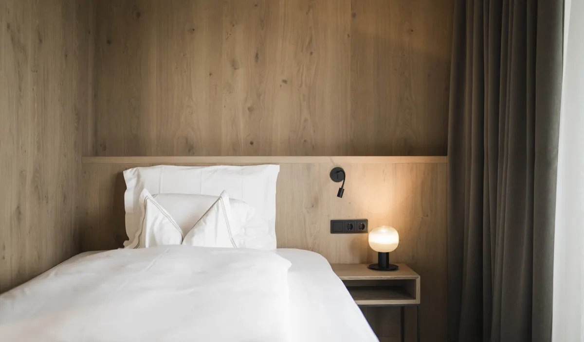 Einzelbett mit weißer Bettwäsche, Nachttisch mit Lampe und Holzwandverkleidung im Zimmer Garden Single Stay.