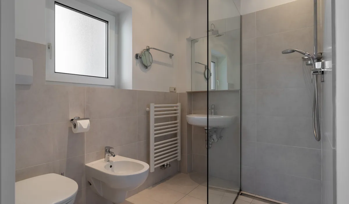 Badezimmer mit ebenerdiger Glasdusche, WC, Bidet, Waschbecken und Handtuchheizkörper.