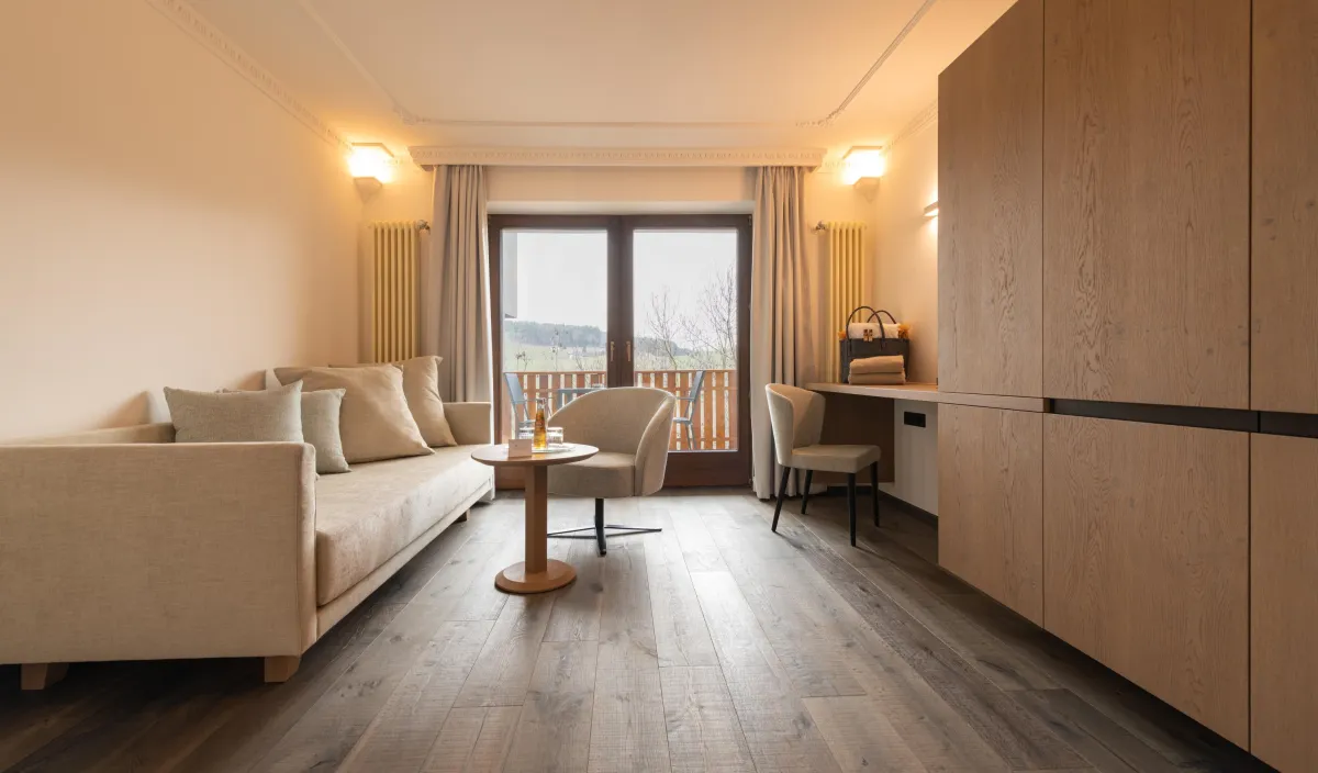 Wohnbereich der Sun Suite mit Sofa, Sessel, Schreibtisch und Balkontür mit Blick ins Grüne.