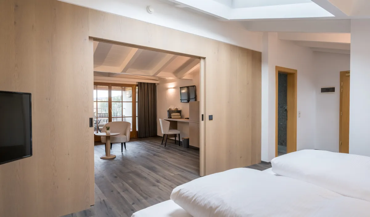 Blick vom Schlafbereich in den Wohnraum mit Sesseln, Schreibtisch und Balkontür der Attico Suite.