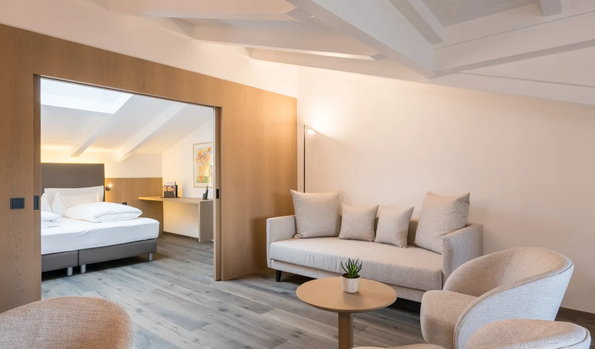 Wohnbereich der Attico Suite mit Sofa, Sessel, Couchtisch und Durchgang zum Schlafzimmer.