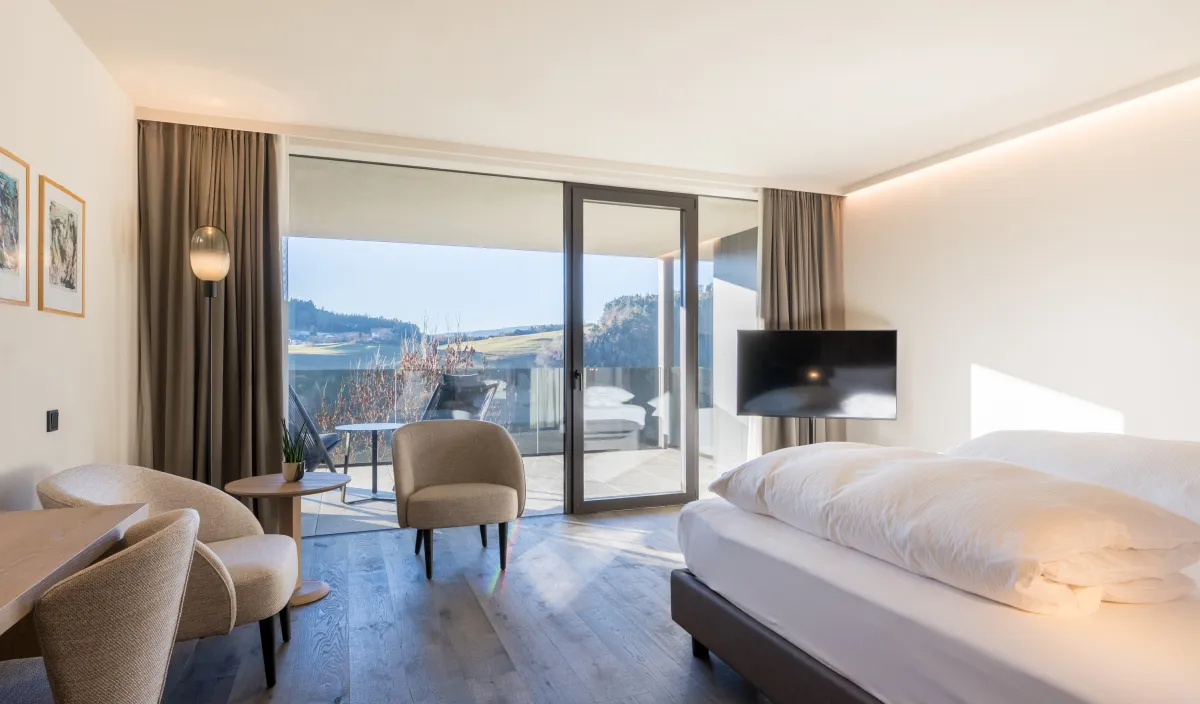 Helles Zimmer Garden View mit Doppelbett, Sesseln, Fernseher und Panoramablick auf die grüne Landschaft.