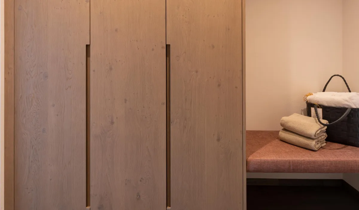 Eingangsbereich mit beleuchtetem Holzschrank, Sitzbank mit Handtüchern und Holz-Wandhaken.