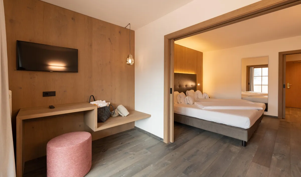 Wohnbereich mit Fernseher, Konsoltisch, rosa Sitzpouf und Durchgang zum Schlafzimmer der Sun Suite.