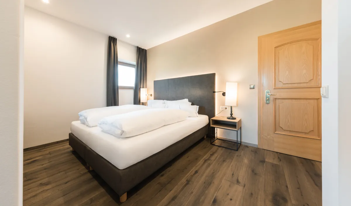 Schlafzimmer mit Doppelbett, Nachttisch, Leselampe und Holztür in der Sun Suite.