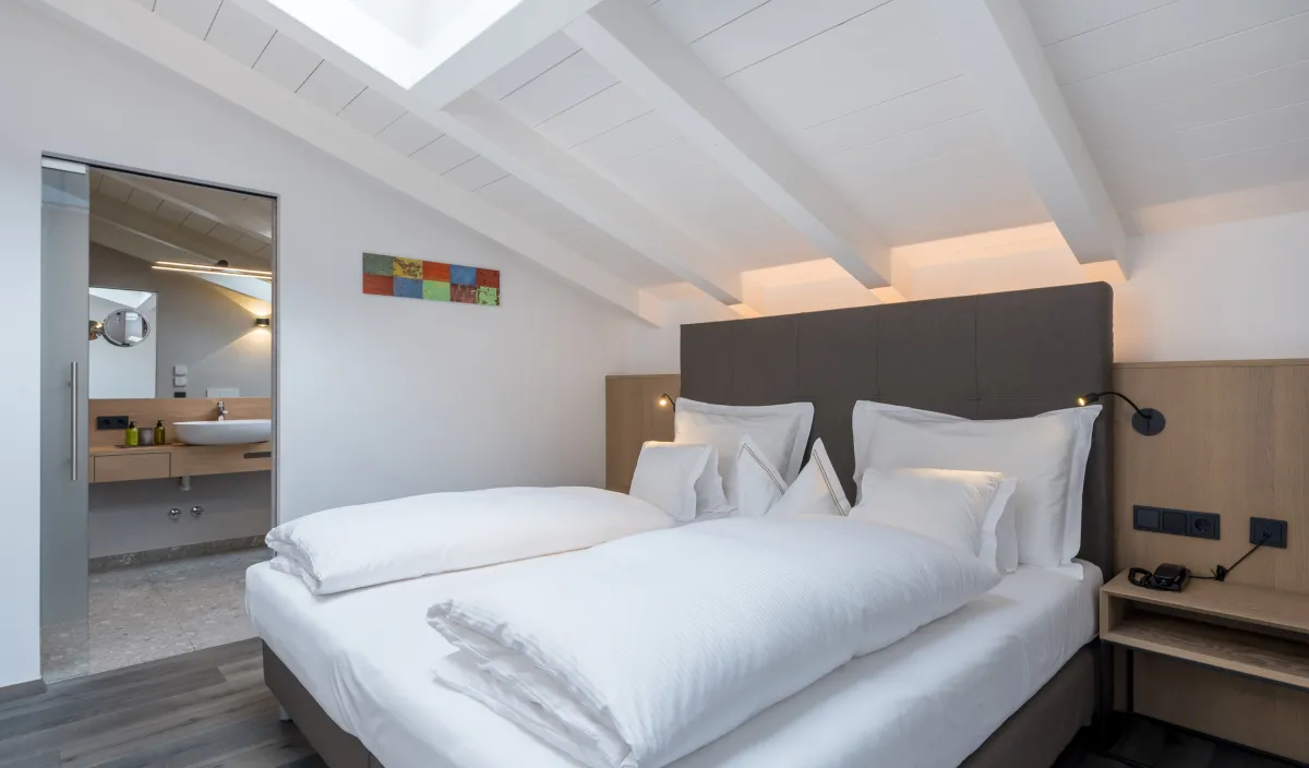 Zweites Schlafzimmer der Attico Suite mit Doppelbett, Dachfenster und offener Badezimmertür.