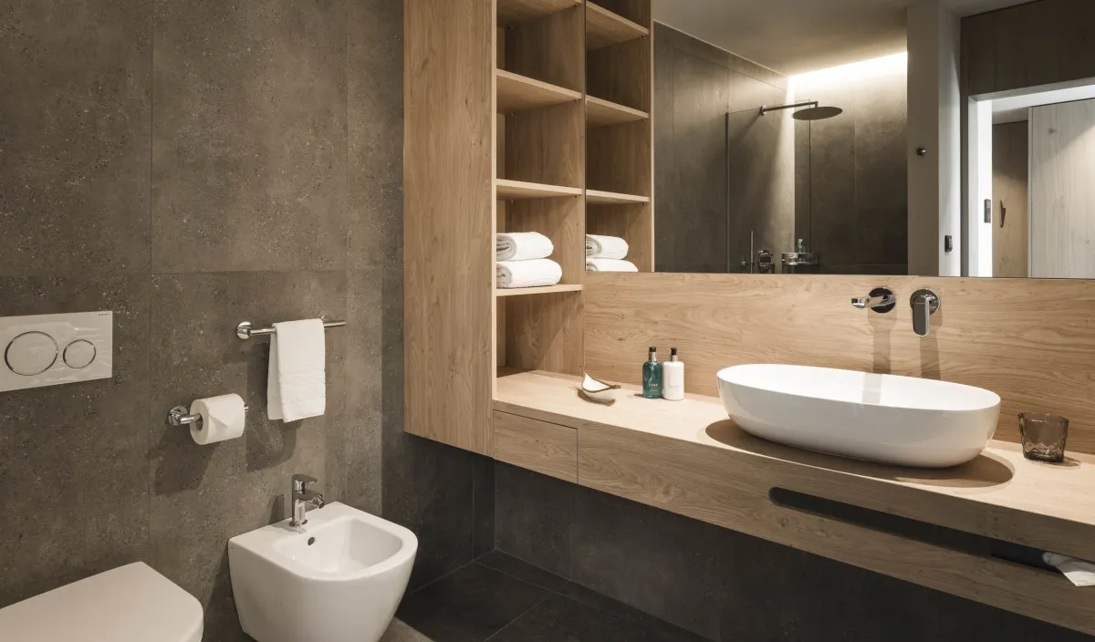 Badezimmer mit Aufsatzwaschbecken auf Holzwaschtisch, Bidet, Handtuchregalen und Regendusche im Spiegel sichtbar.