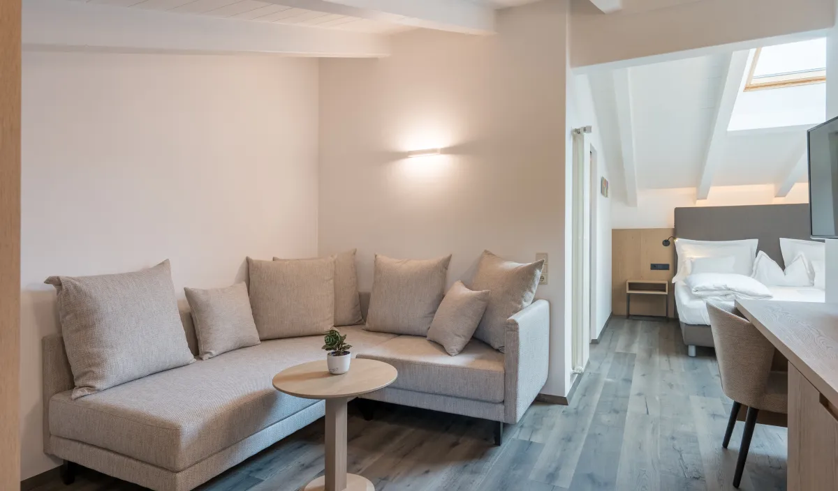 Gemütlicher Wohnbereich mit Ecksofa, Couchtisch und Blick ins Schlafzimmer der Attico Suite.