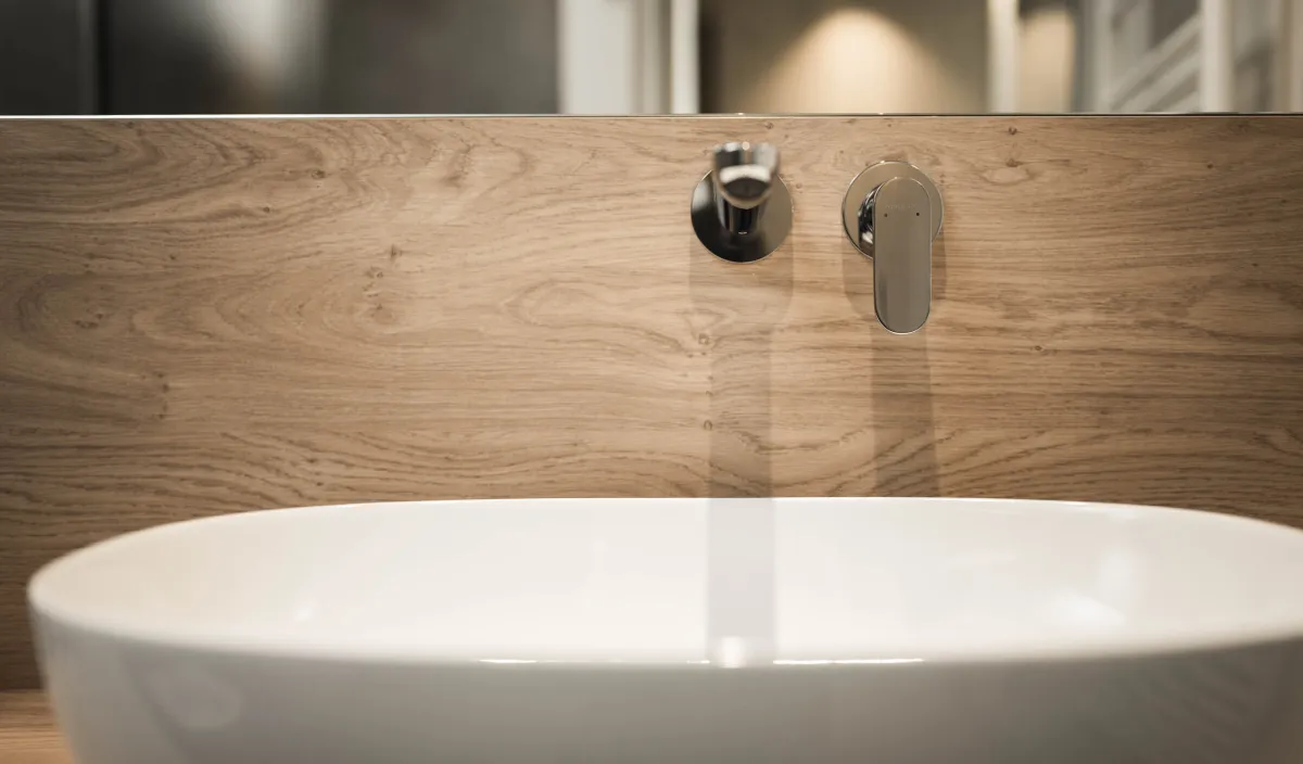 Nahaufnahme des Aufsatzwaschbeckens mit Wandarmatur und Holzrückwand im Badezimmer.
