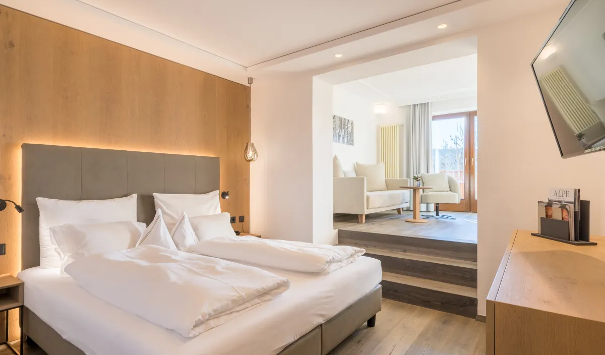 Schlafbereich der Sun Suite mit Doppelbett, Holzrückwand und Stufen zum höher gelegenen Wohnbereich mit Sesseln.