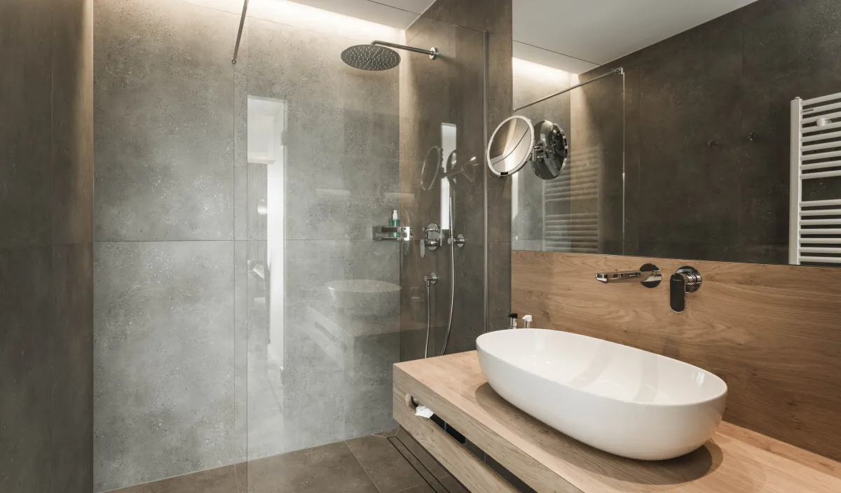 Badezimmer mit begehbarer Regendusche, Aufsatzwaschbecken auf Holzwaschtisch und Natursteinwänden.