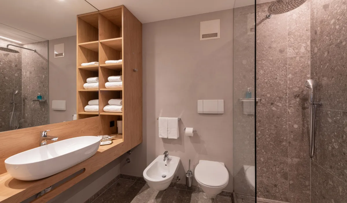 Badezimmer mit Aufsatzwaschbecken auf Holzwaschtisch, Handtuchregalen, Bidet, WC und Regendusche.