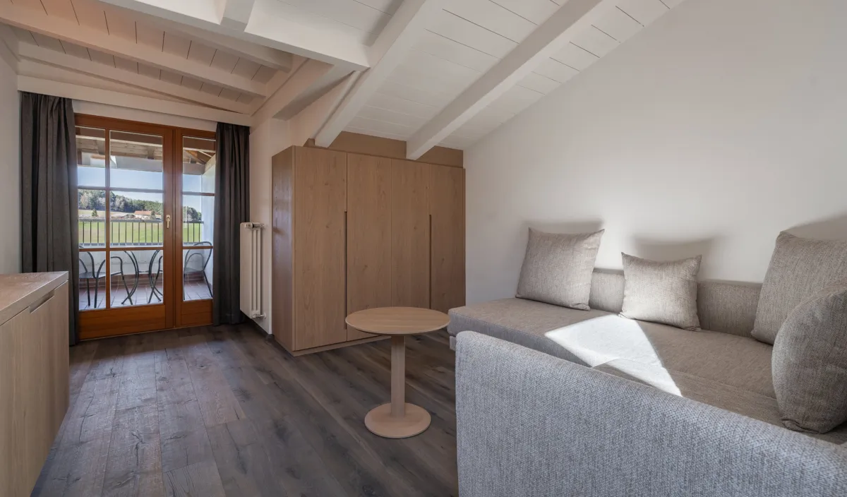Wohnraum mit Sofa, Schrank und Balkontür mit Blick auf die grüne Landschaft in der Attico Suite.
