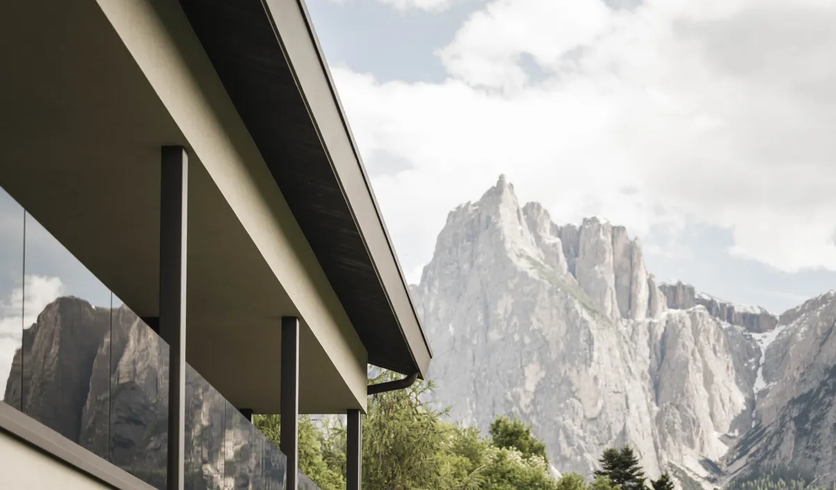 Fassade des Wellnesshotel Alpenflora mit Glasbalkonen und Blick auf die Dolomiten-Felswände.