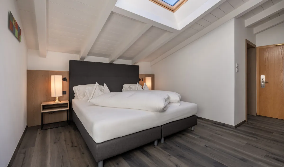Schlafzimmer mit Doppelbett, Nachttischen und offenem Dachfenster mit blauem Himmel in der Attico Suite.