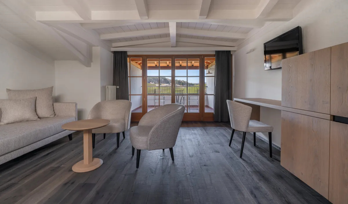Wohnbereich mit Sofa, Sesseln, Schreibtisch und Balkontür mit Panoramablick ins Grüne.