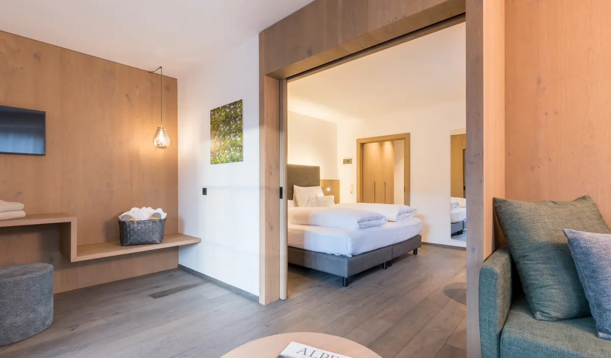 Wohnbereich mit grünem Sofa, Couchtisch, Fernseher und Durchgang zum Schlafzimmer der Sun Suite.