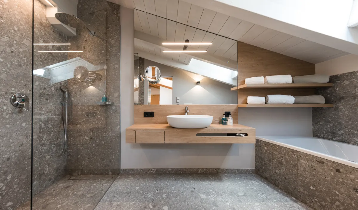 Badezimmer mit begehbarer Dusche, Holzwaschtisch mit Aufsatzwaschbecken und Badewanne unter der Dachschräge.