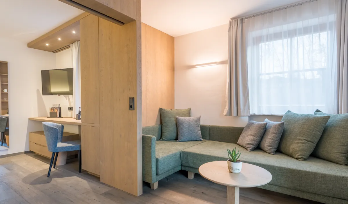 Wohnbereich mit grünem Ecksofa, Couchtisch und Blick durch die Holzschiebetür zum Schreibtisch.