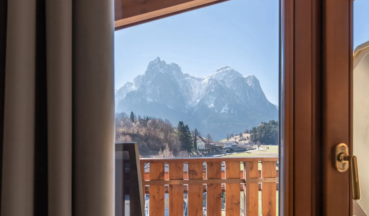 Blick vom Balkon auf die Berge mit Holzgeländer und Vorhang im Vordergrund.