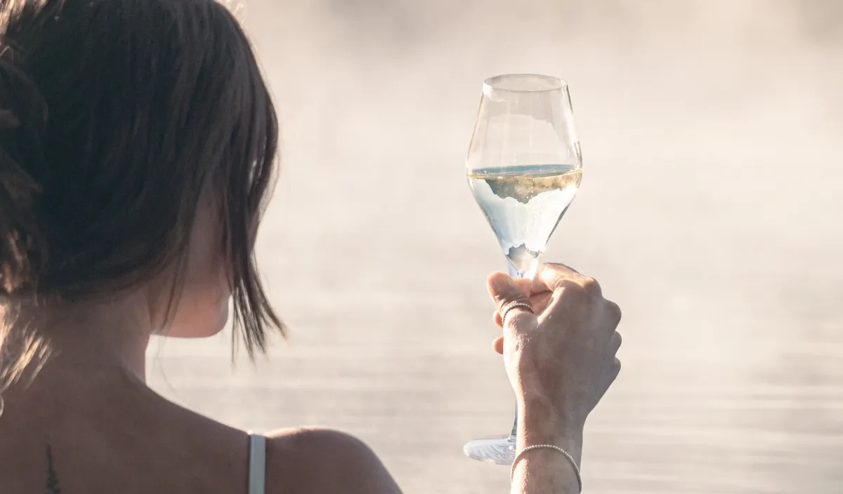 Donna si rilassa nella piscina esterna fumante con un calice di vino bianco in mano.