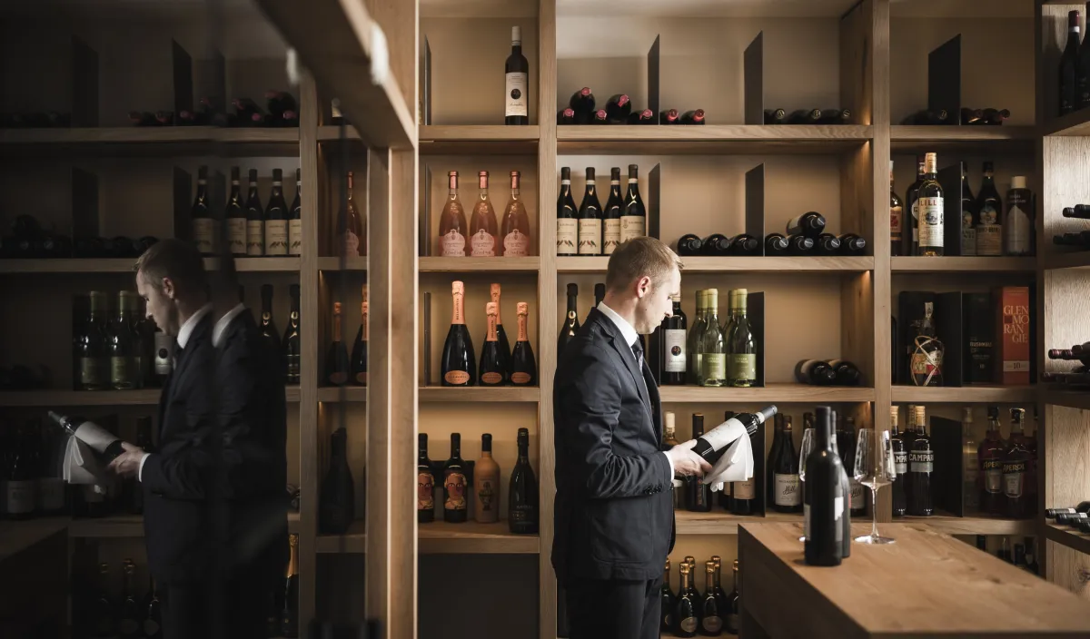Sommelier wählt am gut gefüllten Weinregal des Alpenflora Flaschen aus