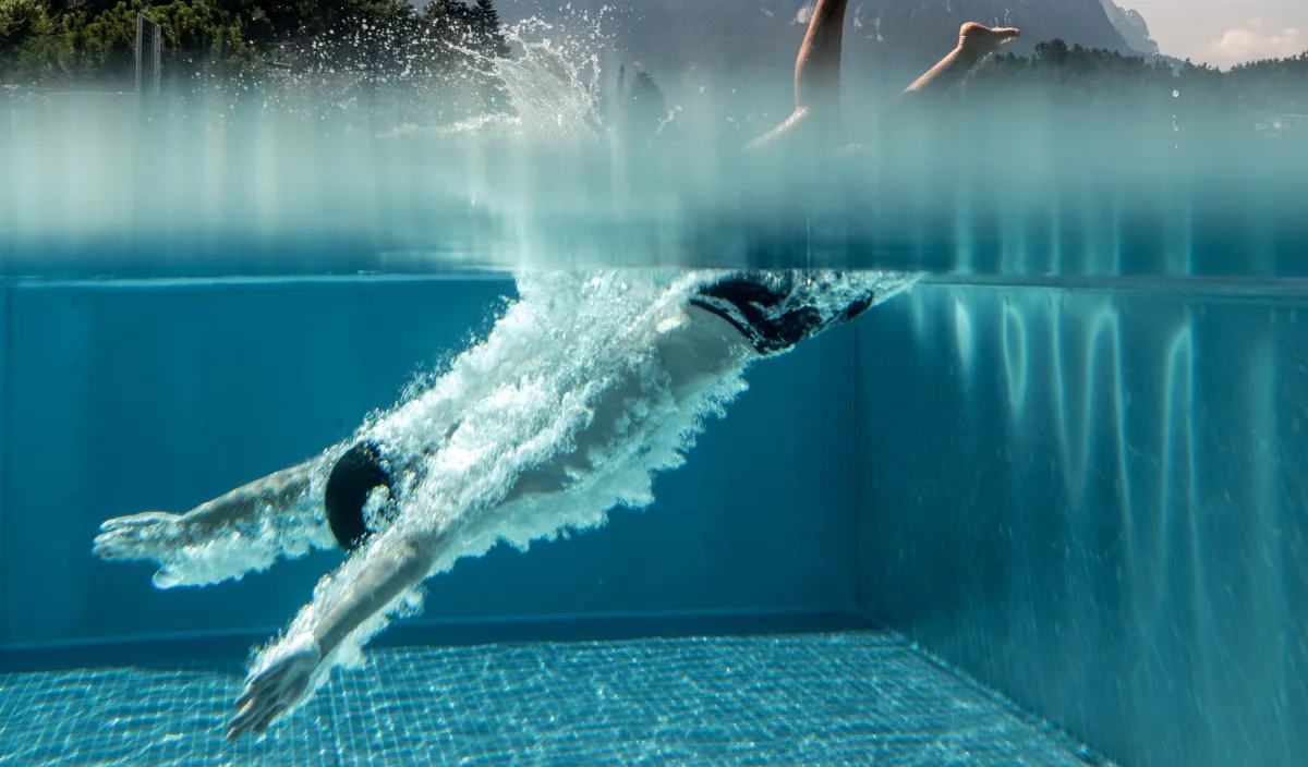 Un nuotatore si tuffa nell’acqua limpida della piscina del Wellnesshotel Alpenflora