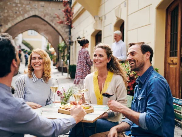 Four people enjoying wine and South Tyrolean specialities at a table under an arcade