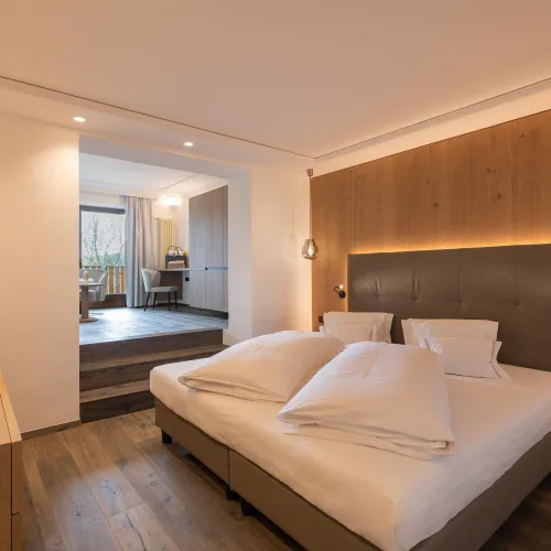 Schlafbereich der Sun Suite im Wellnesshotel Alpenflora mit Doppelbett, Holzwandverkleidung und Durchgang zum Wohnraum.