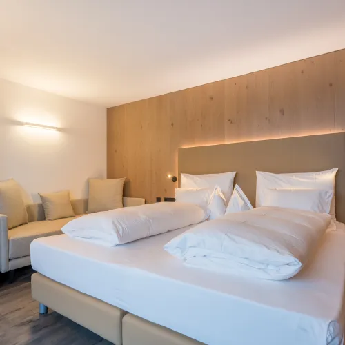 Doppelbett mit gepolstertem Kopfteil, Holzwandverkleidung und Tagesbett mit Kissen im Zimmer Panorama Superior.