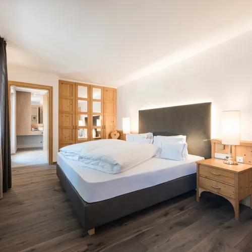 Doppelzimmer Classic mit Doppelbett, Holzschrank mit Glastüren, Nachttischleuchten und Durchgang zum Badezimmer.