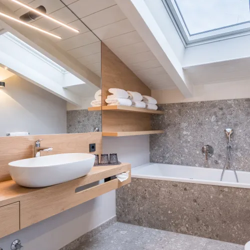Bagno dell'Attico Suite con lavabo d'appoggio, vasca da bagno sotto il tetto spiovente, lucernario e piastrelle in terrazzo.