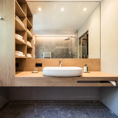 Waschtischbereich der Sun Suite mit Aufsatzwaschbecken, offenem Holzregal mit Handtüchern und Regendusche im Spiegel.
